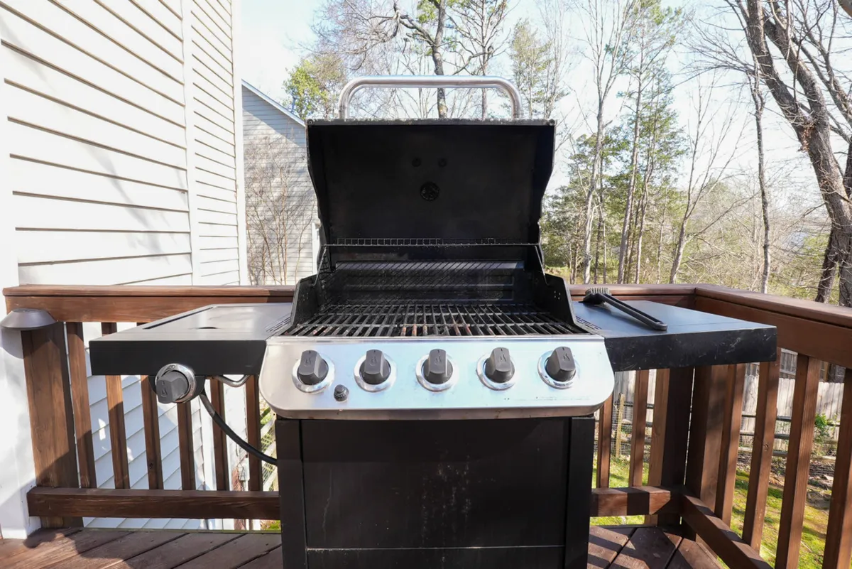 A casual outdoor scene focused on the deck and Charbroil grill, with the surrounding greenery and trees creating a sense of privacy and natural beauty. The deck is perfect for barbecues, social gatherings, and relaxing summer evenings.