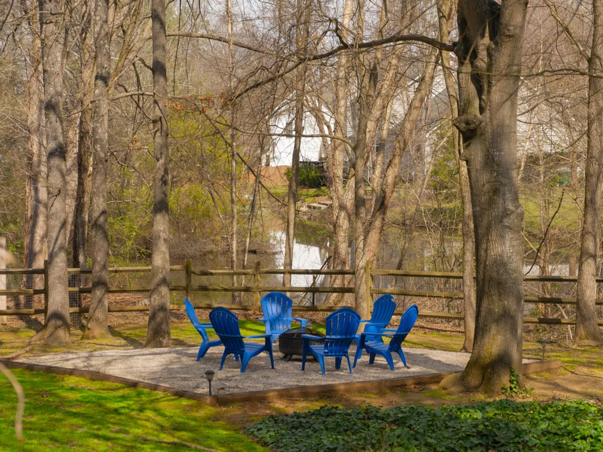 An inviting backyard setting with blue chairs arranged around a fire pit, surrounded by trees. The fire pit area suggests a perfect spot for evening relaxation, roasting marshmallows, and sharing stories under the stars.