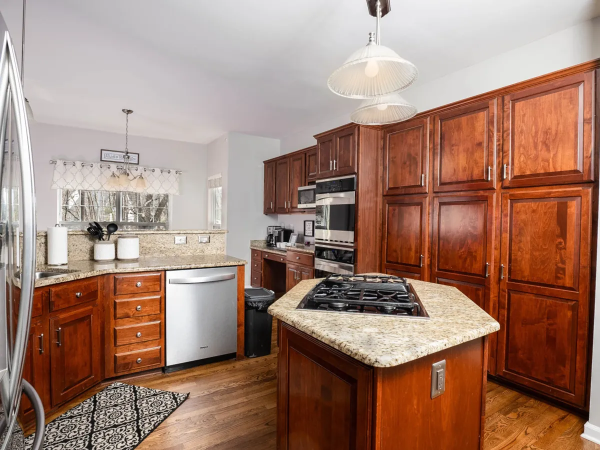 A view of the kitchen with granite countertops, wood cabinetry, stainless steel appliances, and a central island. The layout is open and inviting, suited for both cooking and socializing with family or friends.