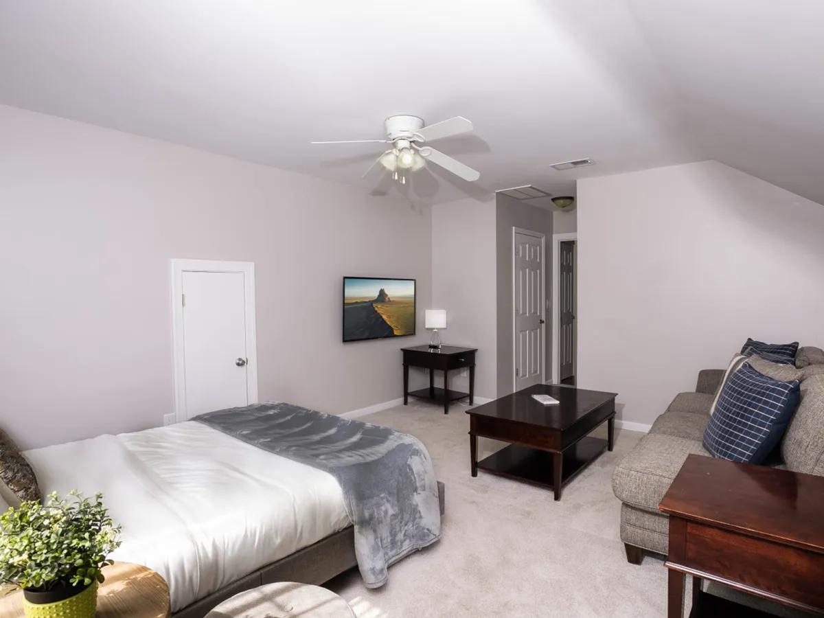 An inviting living area featuring a bed with a gray blanket, a comfortable sofa, coffee table, TV displaying a scenic image, and a warm lamp. The mood is cozy and intimate, ideal for unwinding together after city adventures.