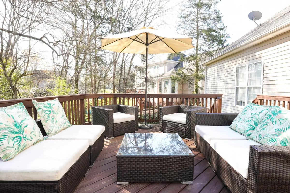 The hero image showcases a private backyard oasis with a spacious outdoor seating area under a large umbrella, surrounded by lush trees. A coffee table invites guests to gather and relax, while the golden hues of sunset filter through the foliage, creating a serene and inviting setting perfect for sipping drinks, socializing, or unwinding with a good book.
