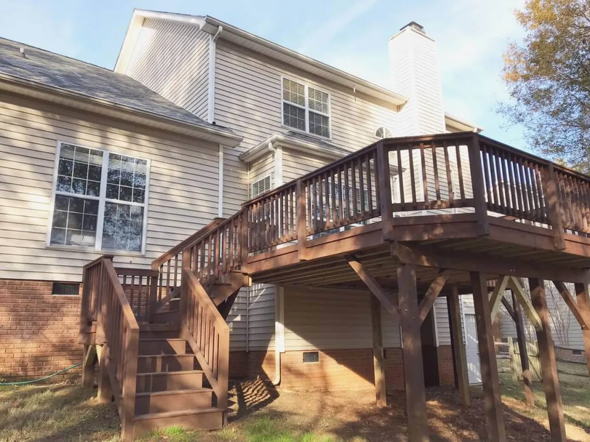 A spacious wooden deck with a staircase leading down to a brick foundation, large windows, and comfortable seating. The deck area is ideal for barbecues, relaxing in the fresh air, or enjoying sunset dinners with family.