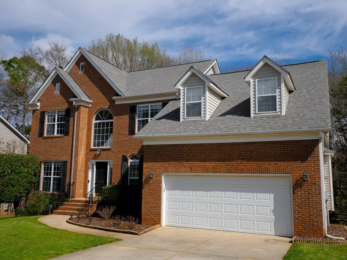 This exterior image showcases a brick facade with large windows, a landscaped garden, front steps, and a garage door. The scene conveys a sense of welcoming arrival and hints at spaces for outdoor family activities, such as gatherings, gardening, or barbecues.