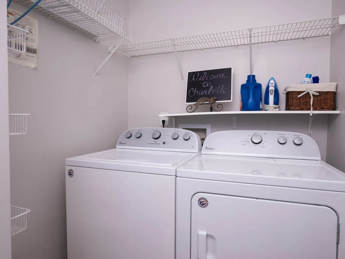 A well-organized laundry area with a washer and dryer, a chalkboard sign, and storage shelves for supplies, creating a functional yet welcoming atmosphere. The space is designed for convenience and efficient household routines.